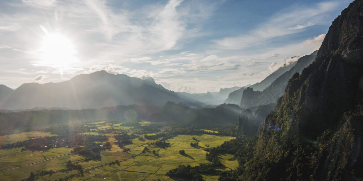 A wide-angle view of rugged mountains and lush farmland in Laos taken from a high peak, showcasing the image quality possible with a modern travel camera.