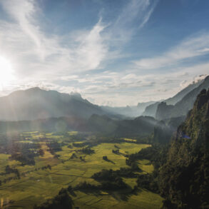 A wide-angle view of rugged mountains and lush farmland in Laos taken from a high peak, showcasing the image quality possible with a modern travel camera.