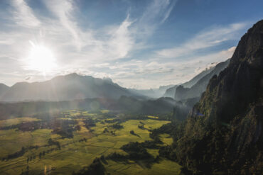 A wide-angle view of rugged mountains and lush farmland in Laos taken from a high peak, showcasing the image quality possible with a modern travel camera.