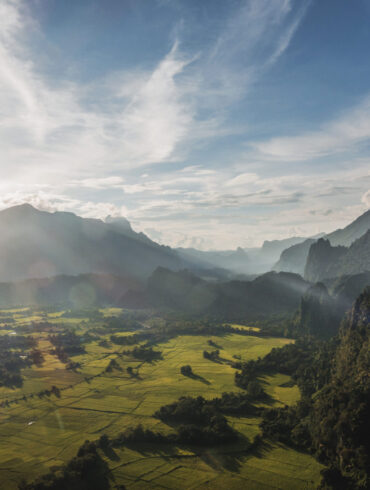 A wide-angle view of rugged mountains and lush farmland in Laos taken from a high peak, showcasing the image quality possible with a modern travel camera.