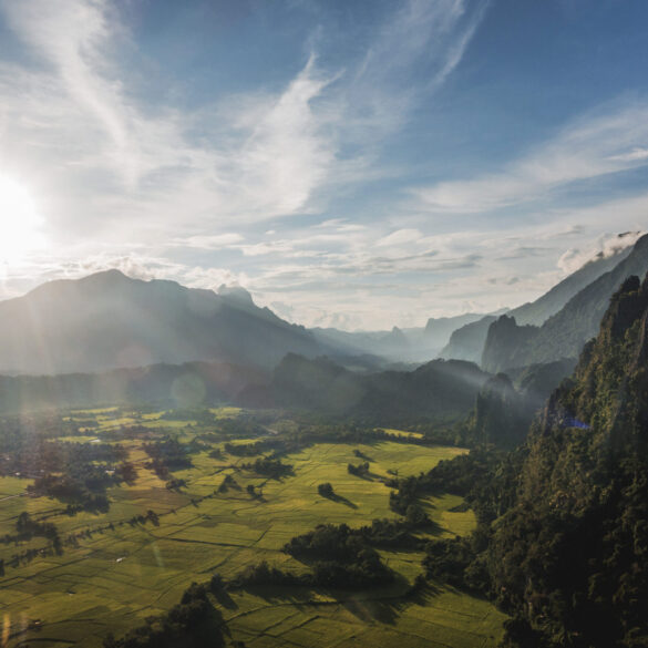 A wide-angle view of rugged mountains and lush farmland in Laos taken from a high peak, showcasing the image quality possible with a modern travel camera.
