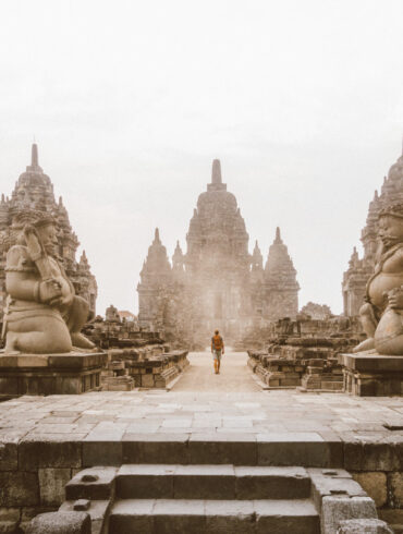 Traveler walking near an ancient temple in Indonesia, carrying a backpack and a Sawyer water bottle. Southeast Asia travel photography.